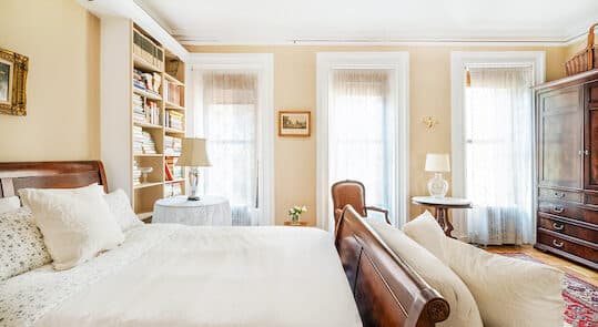 Bedroom with brown sleigh bed with white bedding. 3 windows and sofa.