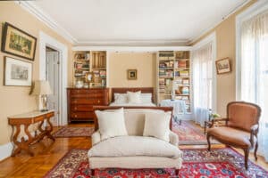 Bedroom with brown sleigh bed. White bedding. Sofa at foot of bed. Red rugs.